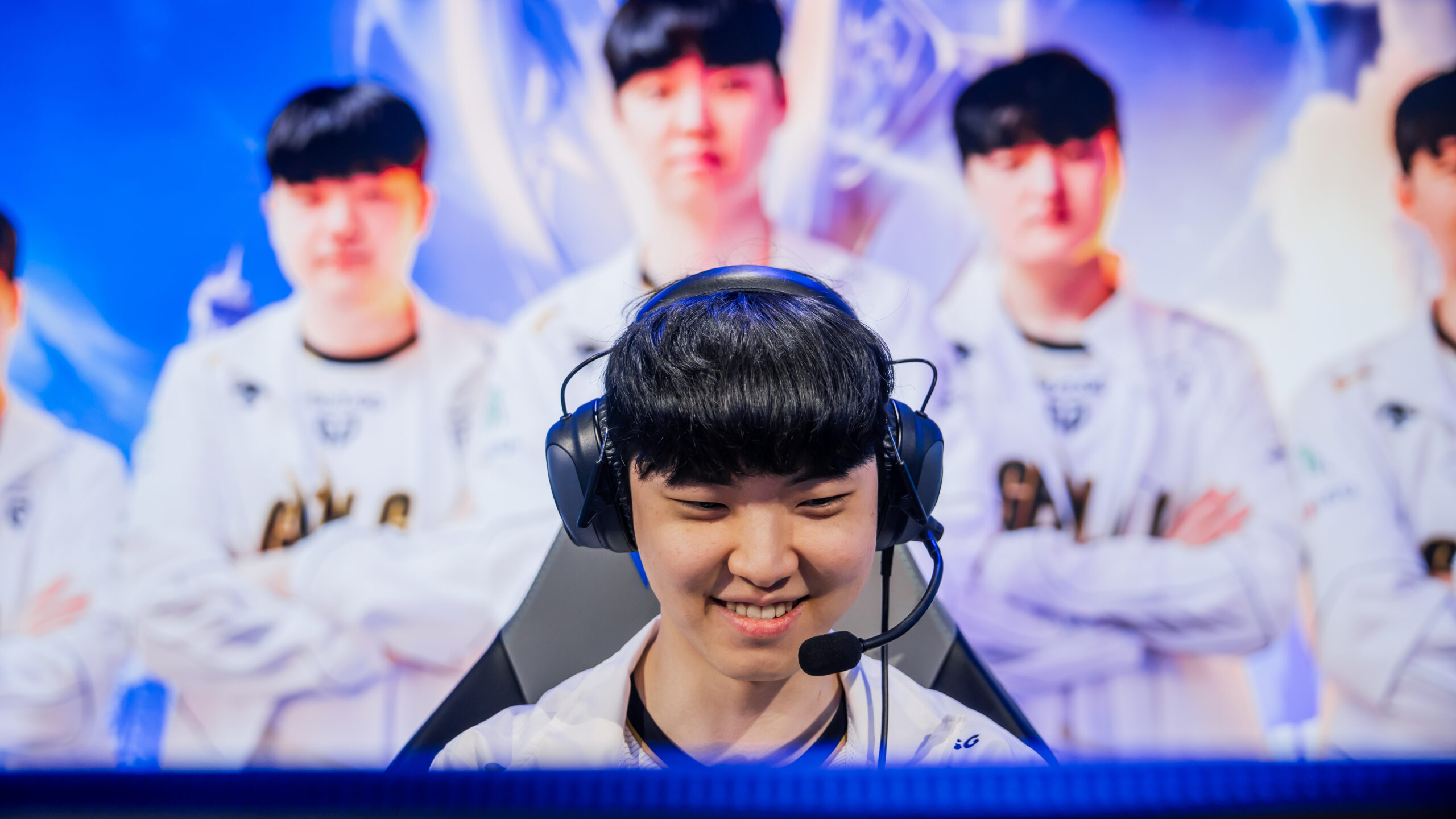 foto do mid laner Chovy da GenG sorrindo como time aparecendo atrás no palco do Worlds LoL 2024