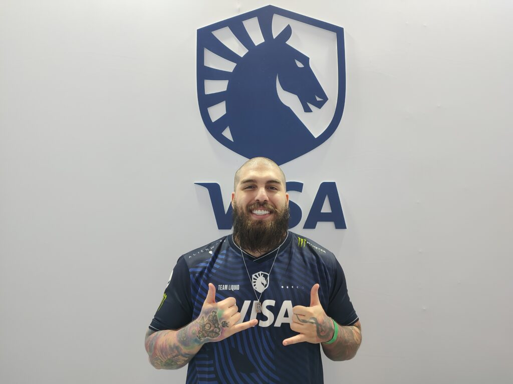 ex jogador de lol Rakin posando para foto em frente à logo da Team Liquid na CCXP